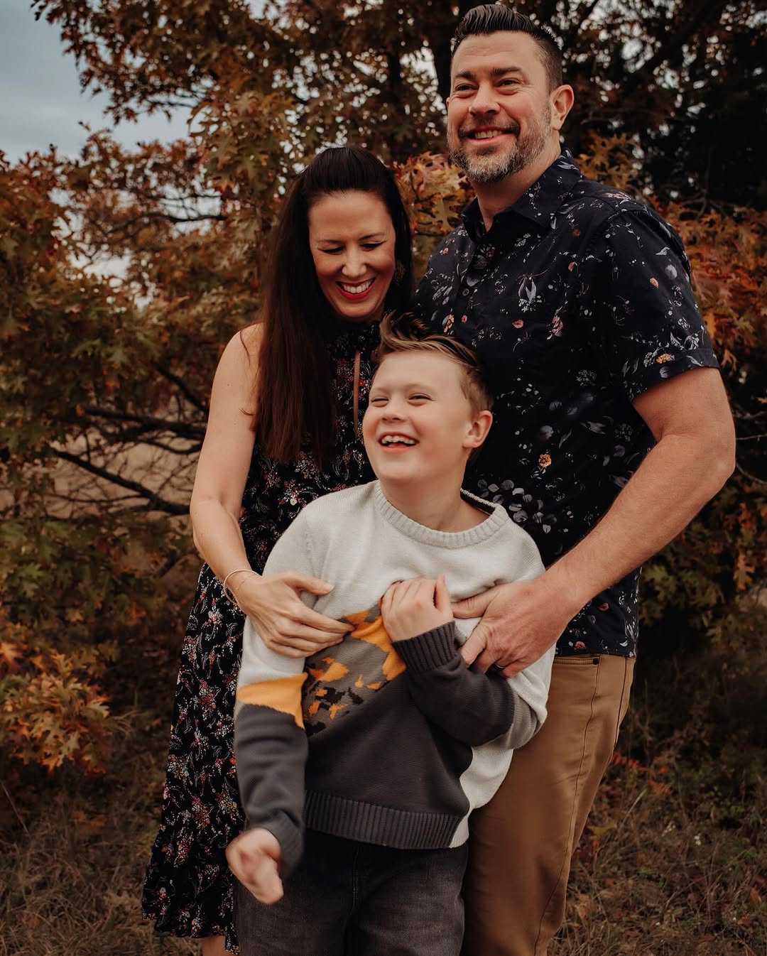 Family of three laughing together under fall trees